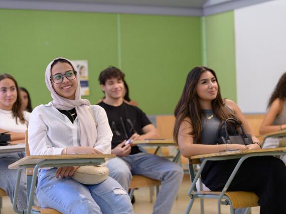 AUC students sit at desks in a classroom with a green wall behind them