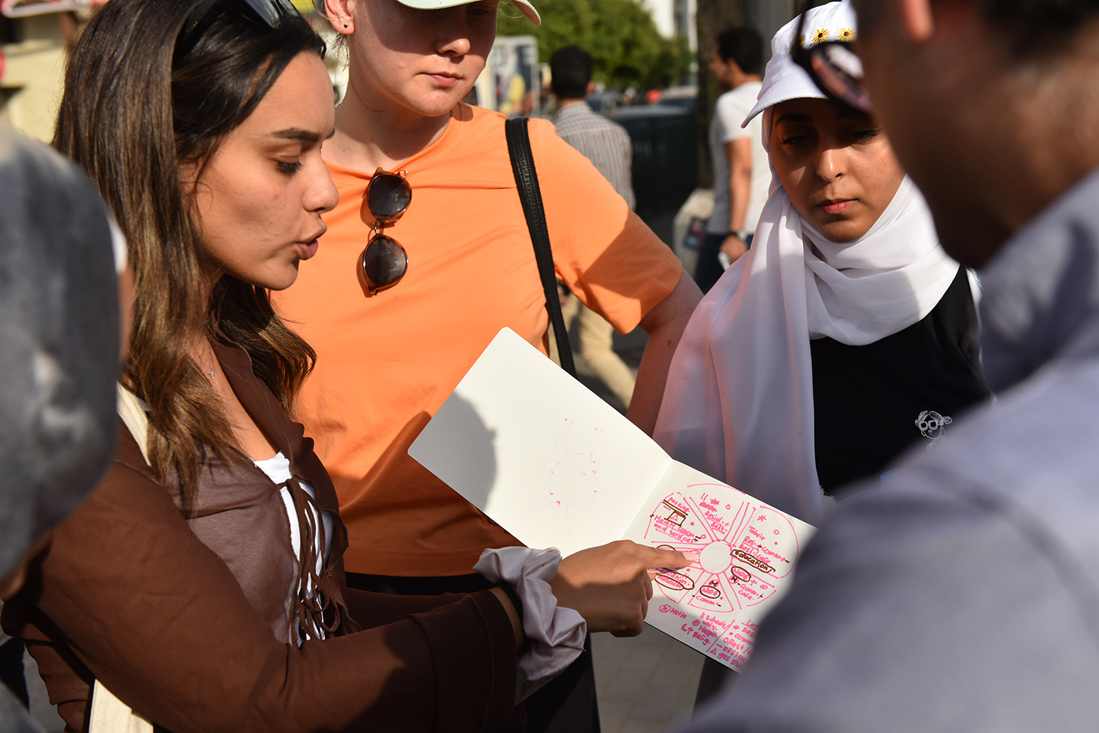 A girl holding a paper and pointing at it while explaining to a group of people
