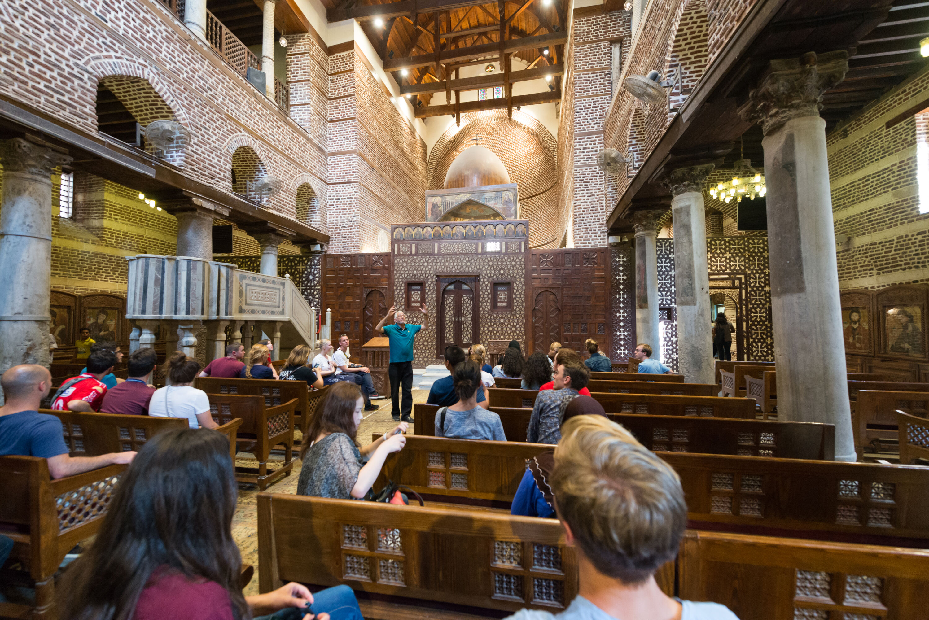 A group of international students sitting inside a church listening to a guide explaining