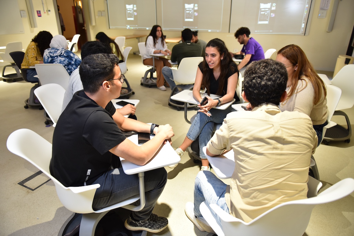 Students sit in small groups in a classroom discussing ideas and working together.