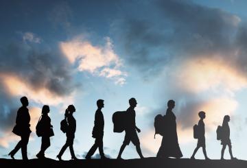 Silhouette of people walking in a line with the sky illuminated behind them