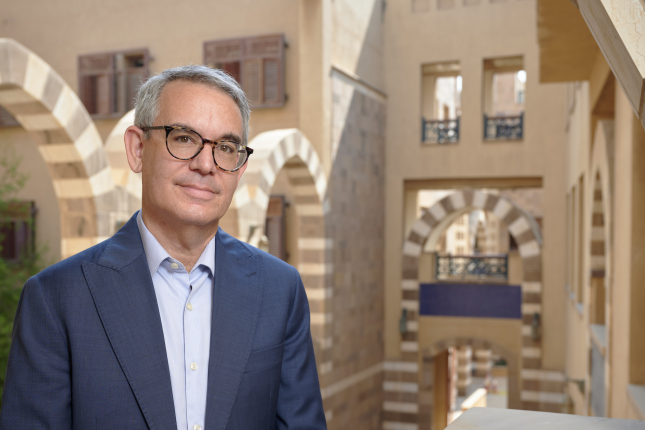a man wearing a suit and glasses, standing in the architecturally hollow space inside the HUSS building
