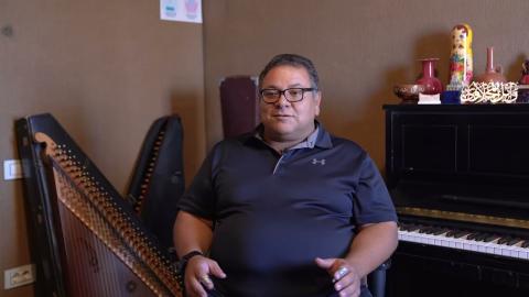 A male is sitting down between a piano and a harp