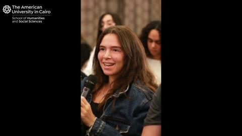 A female is talking into a microphone. Text: The American University in Cairo. School of Humanities and Social Sciences