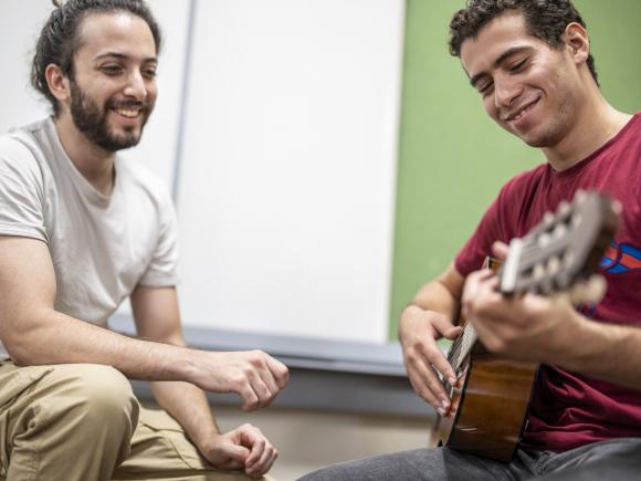 student learning to play the guitar with his instructor