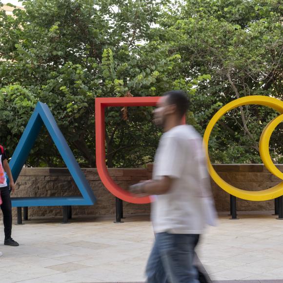 AUC large logo on AUC campus with students walking past it