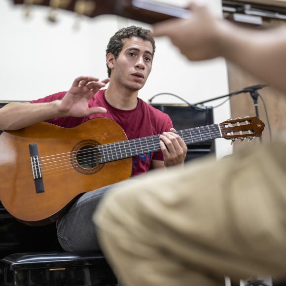 student learning to play the guitar with a professor in a studio