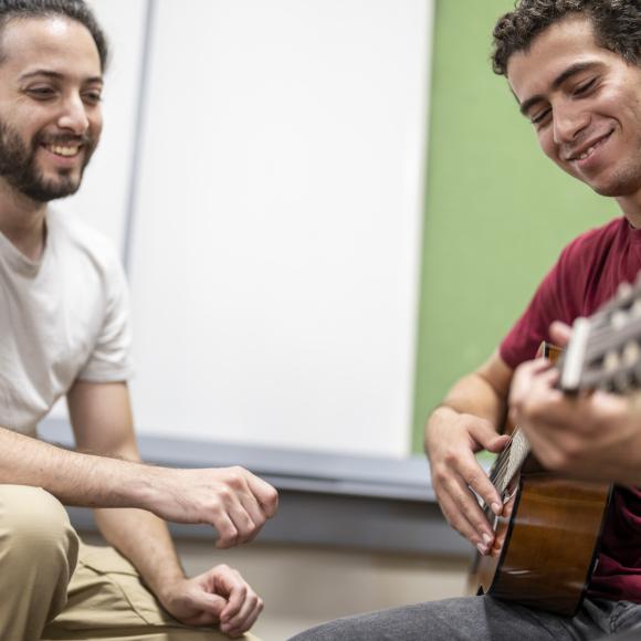 student working with faculty on playing guitar 