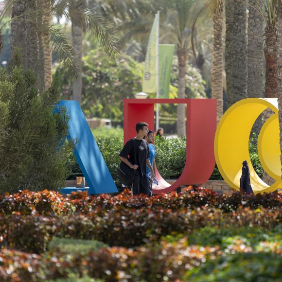 student walking in auc garden next to large auc logo